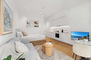 Ein modernes, helles Zimmer mit Bett, Sofa, Fernseher und Küchenzeile.