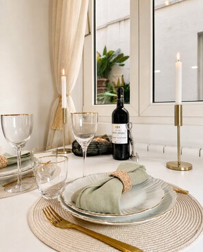 Une table à manger dressée avec des assiettes, des verres, des couverts, une bouteille de vin et des bougies.