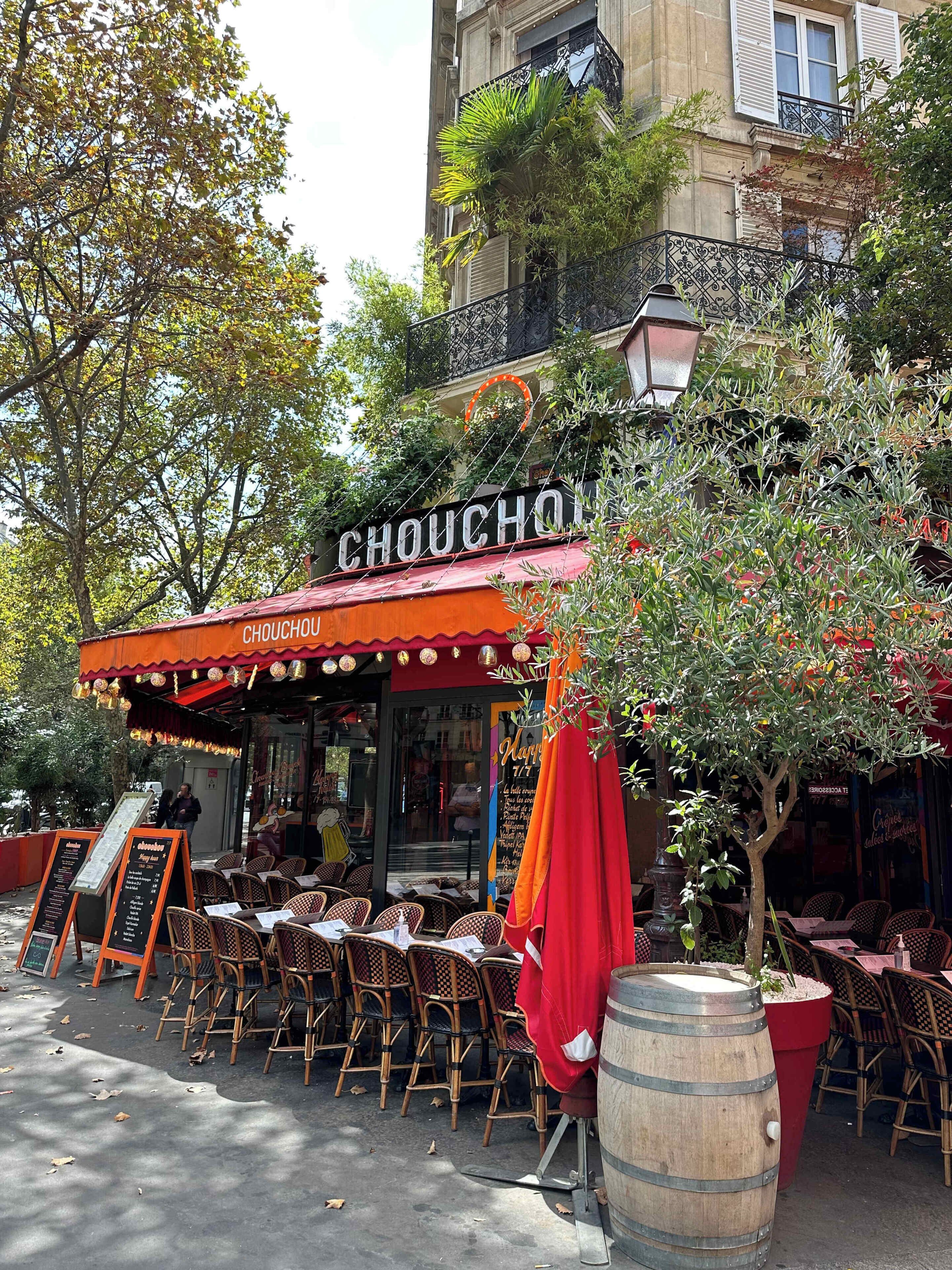 Un café en plein air avec un auvent rouge, des tables à l’extérieur et un panneau affichant le menu.