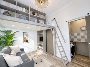 A modern living space with a loft area, a sofa, a coffee table, a ladder, and a washing machine. - Stylish studio near the Tuileries Gardens (Paris)