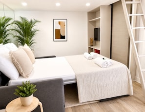 Une chambre d’hôtel moderne avec un lit, une petite table sur laquelle est posée une plante, une échelle et un tableau accroché au mur.