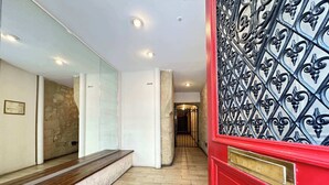 Un couloir avec une porte rouge, un escalier et un mur en pierre.