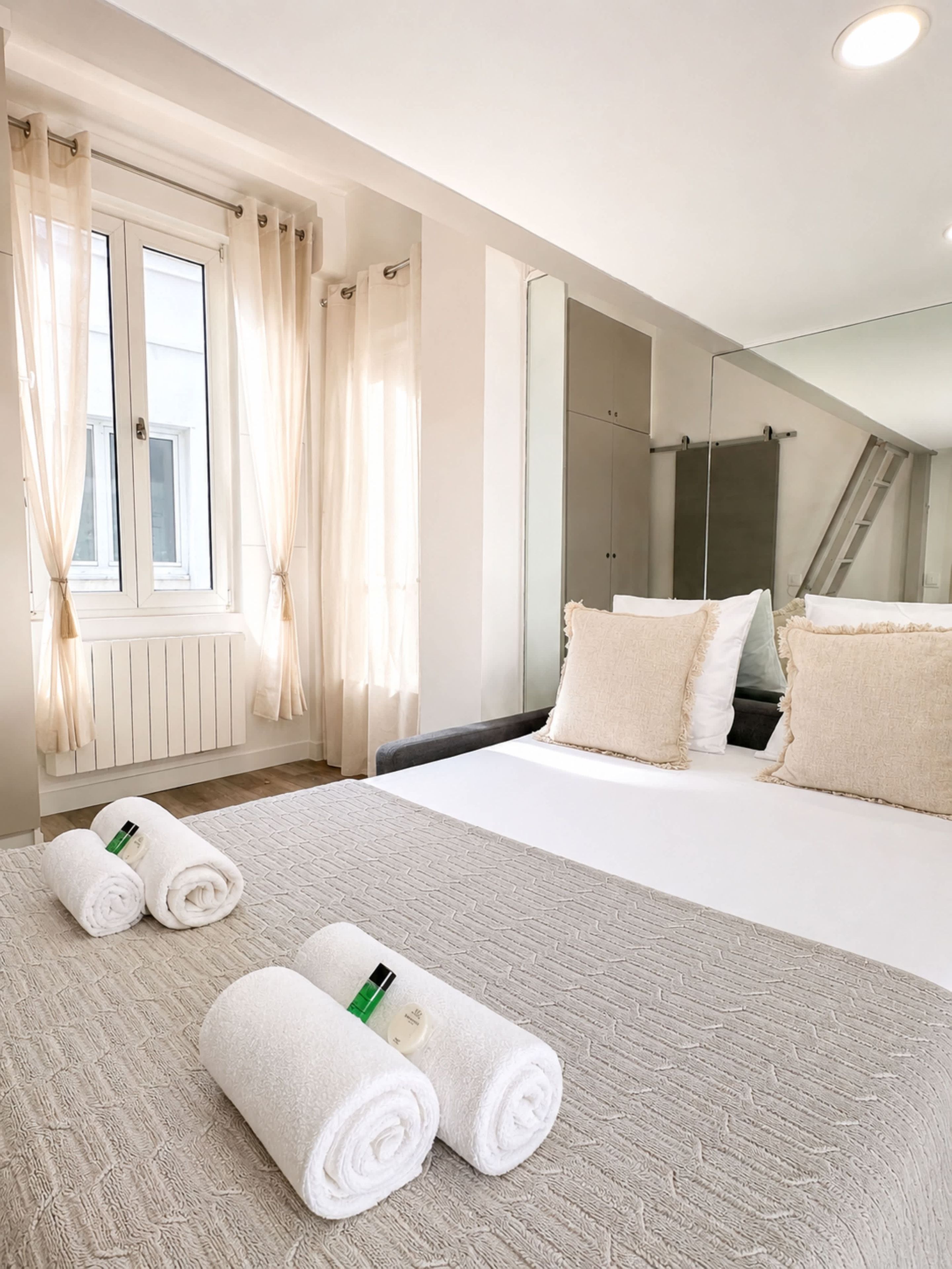 A hotel room with a large bed, a window with curtains, a mirror, and a radiator.