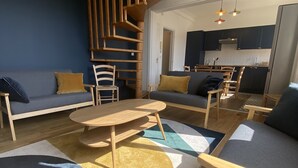 A modern living room with a wooden staircase, a dining area, and a kitchen.