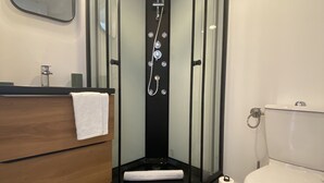 A modern bathroom with a glass-enclosed shower, a wooden vanity, a toilet, and patterned floor tiles.