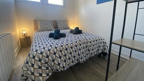 A bedroom with a patterned bedspread, two bedside lamps, a radiator, and a wall art piece.