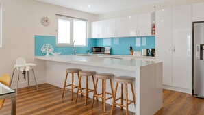 Una cocina moderna con armarios blancos, una pared azul de acento, una isla grande con taburetes y un refrigerador de acero inoxidable.