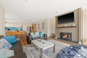 A modern living room with a fireplace, a flat-screen TV, and a dining area with orange chairs.