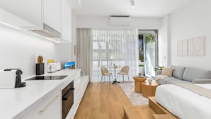 Cocina moderna con encimera, tostadora y pileta. Hay un comedor con mesa y sillas. Se ven un sofá y una cama al fondo.