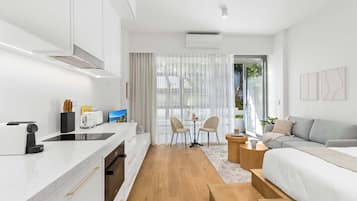 Une cuisine moderne avec un plan de travail, un grille-pain et un évier. On y trouve également un coin repas avec une table et des chaises. Un canapé et un lit sont visibles au fond de la pièce.