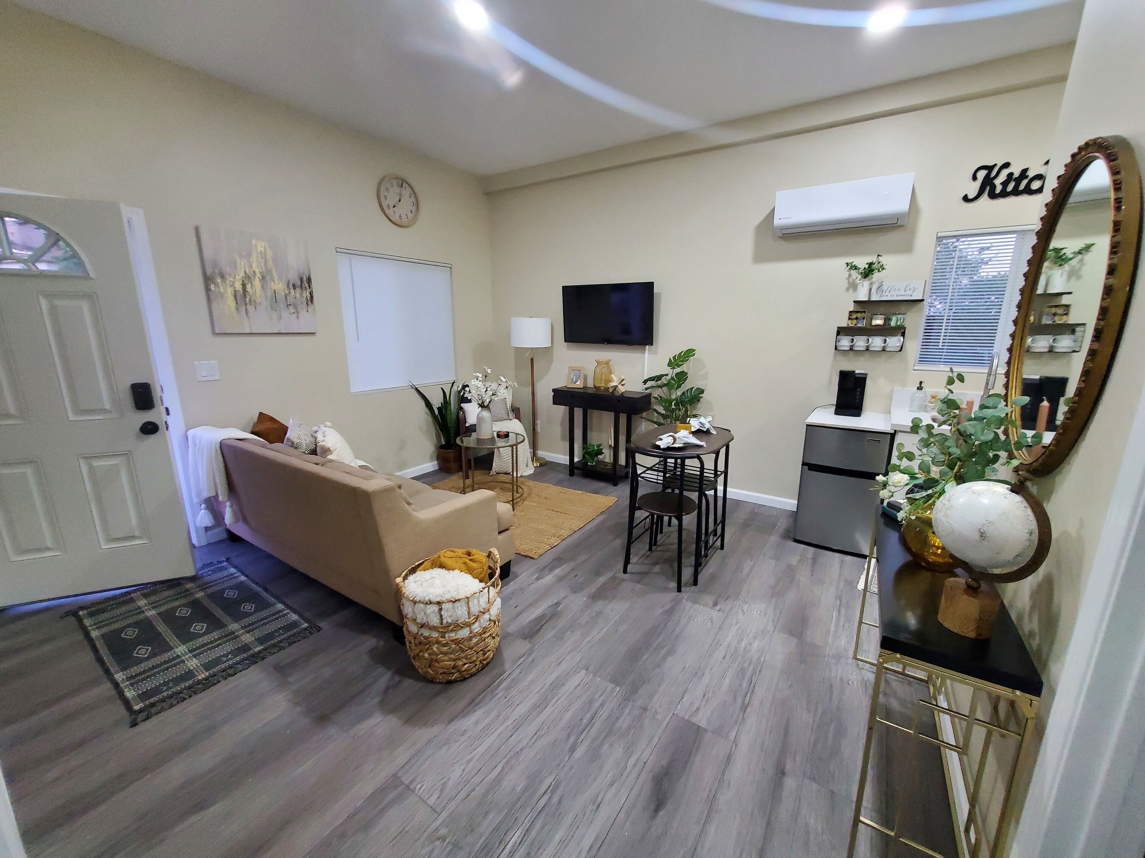 A living room with a sofa, a coffee table, a dining table, and a kitchen area with a refrigerator and a sink.