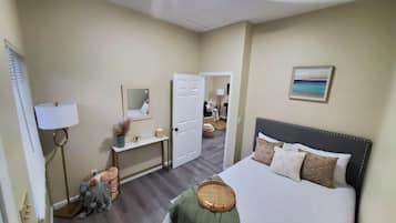 A hotel room with a bed, bedside table, lamp, mirror, and a painting on the wall.