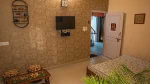 Un dormitorio con cama, televisor, estante con adornos y una puerta que da a otra habitación.