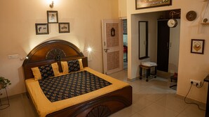 Un dormitorio con cama de madera, una mesita de noche, un reloj en la pared y una puerta que da a otra habitación.