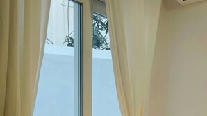 Une pièce avec une grande fenêtre, une petite table sur laquelle est posée une plante, et une lampe.