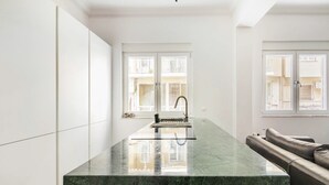 Une cuisine moderne dotée d’un îlot en marbre, de meubles blancs et offrant une vue dégagée grâce à de grandes fenêtres.