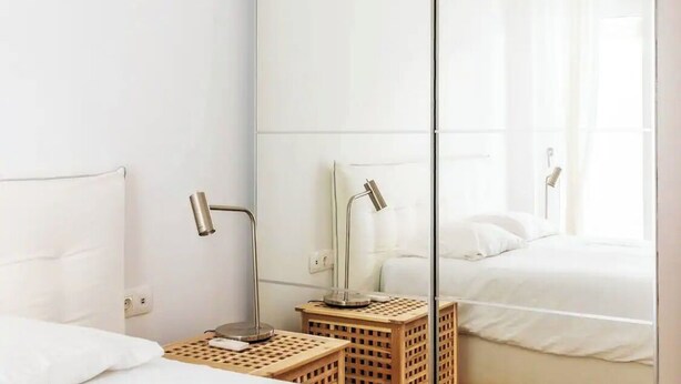 Une chambre d’hôtel avec un mur miroir, un lit, une table de chevet avec une lampe et un petit tabouret en bois.