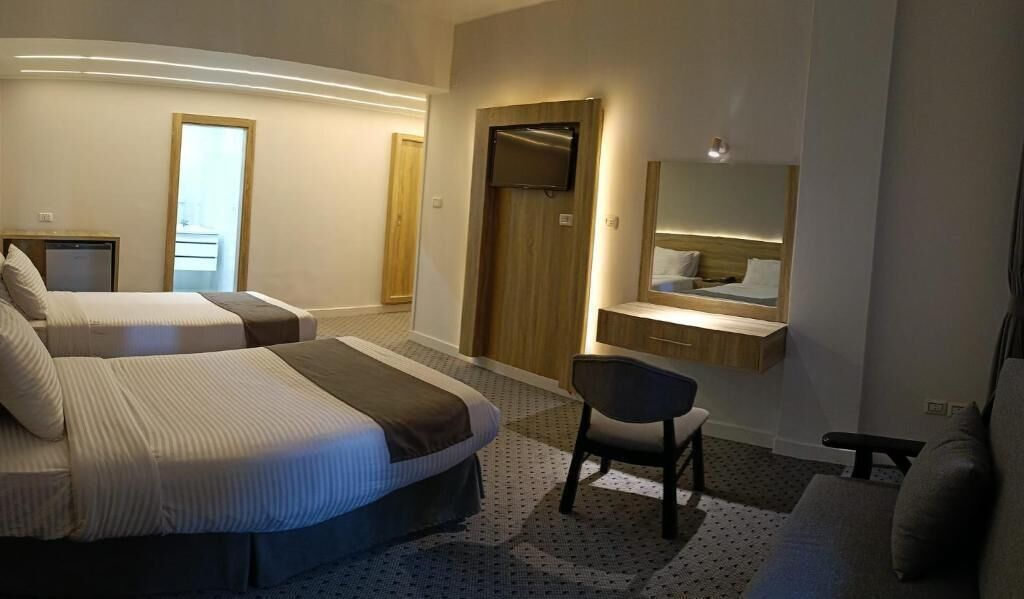 A hotel room with two beds, a desk, a chair, a TV, and a mirror.