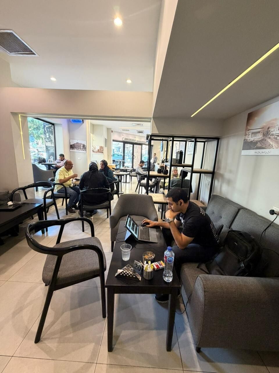 A modern indoor space with seating arrangements, tables, and a person using a laptop.