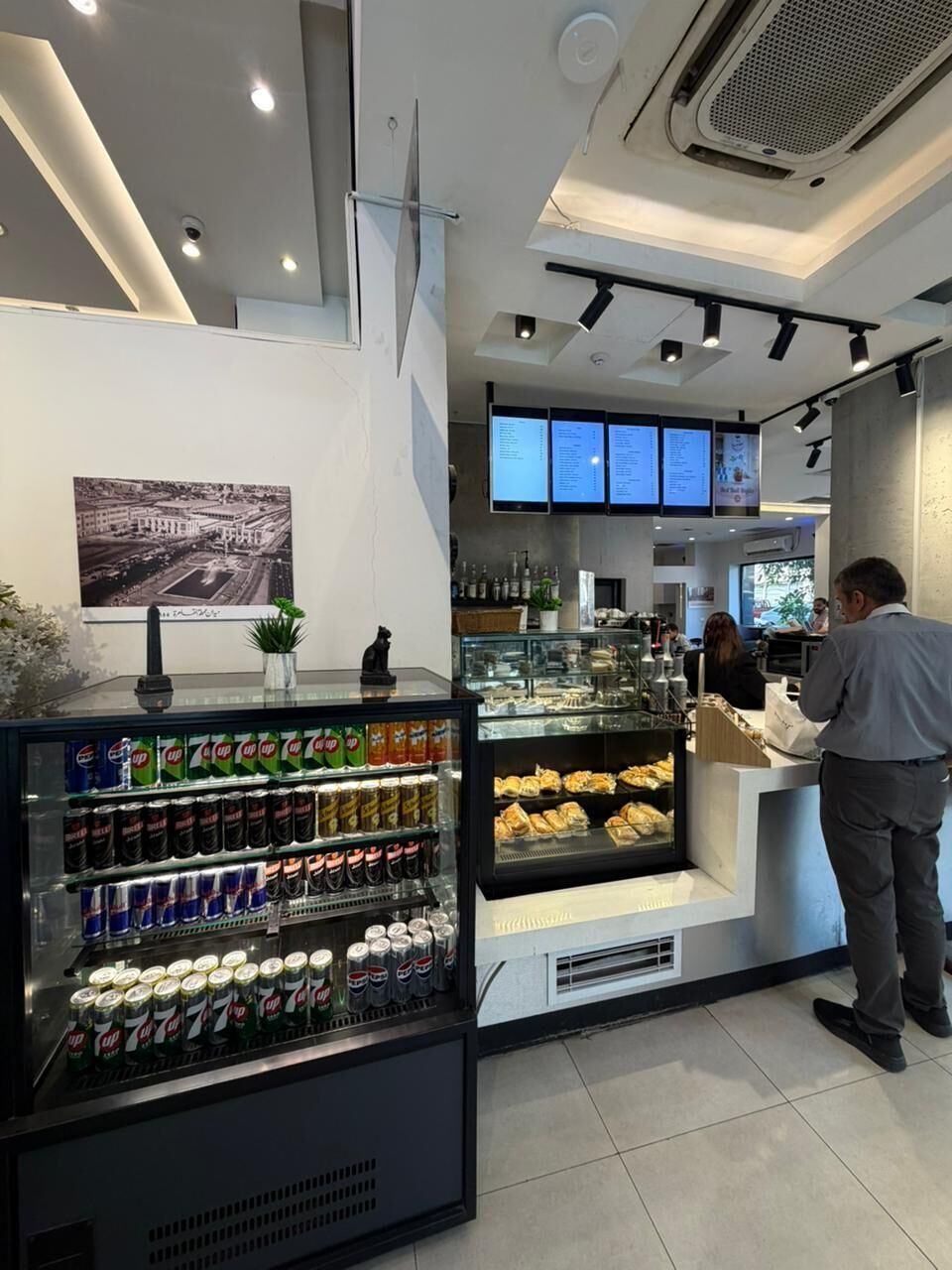 A café interior with a beverage dispenser, a display case with pastries, and a menu board.