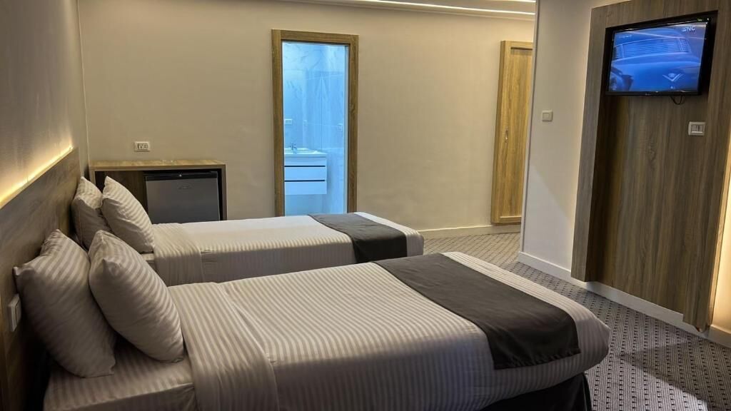 Habitación de hotel con dos camas, televisor, escritorio y puerta corrediza a un balcón.