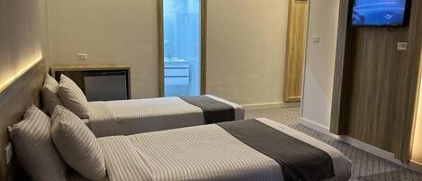 Habitación de hotel con dos camas, televisor, escritorio y puerta corrediza a un balcón.