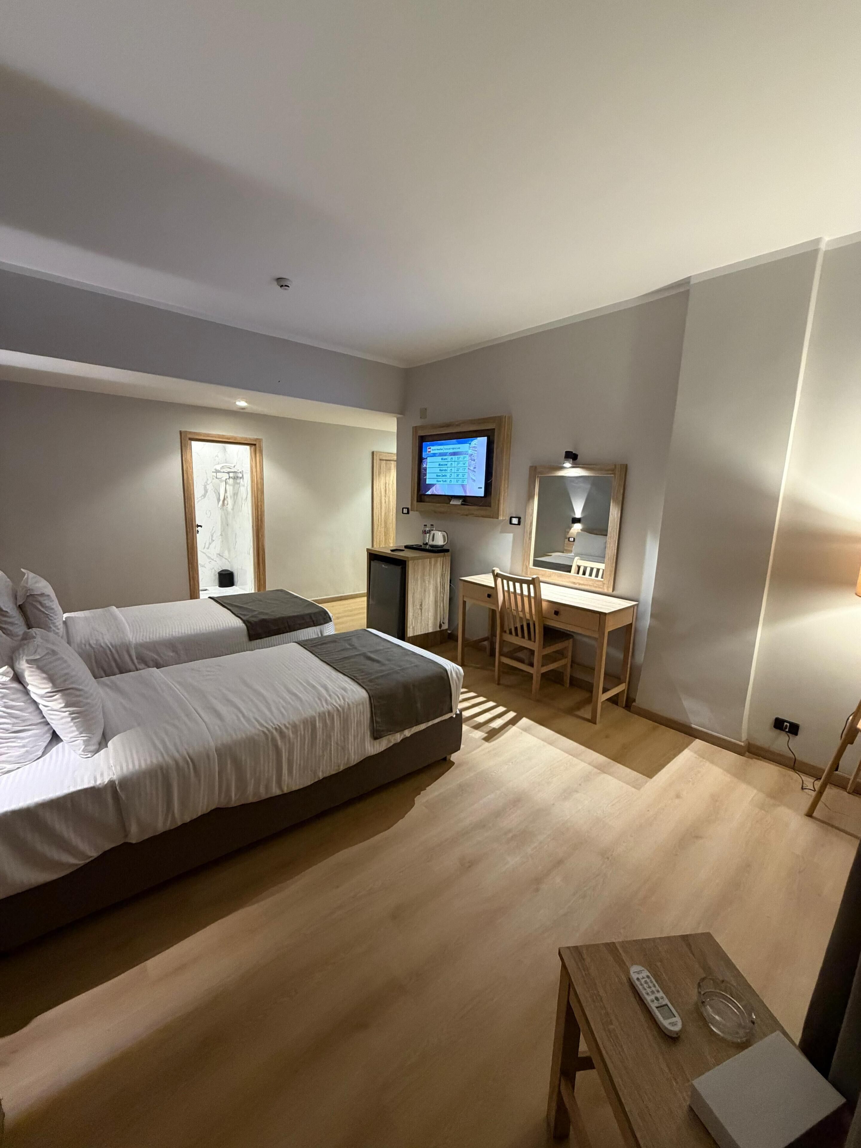 A hotel room with a bed, desk, chair, TV, and a small table with a remote control.
