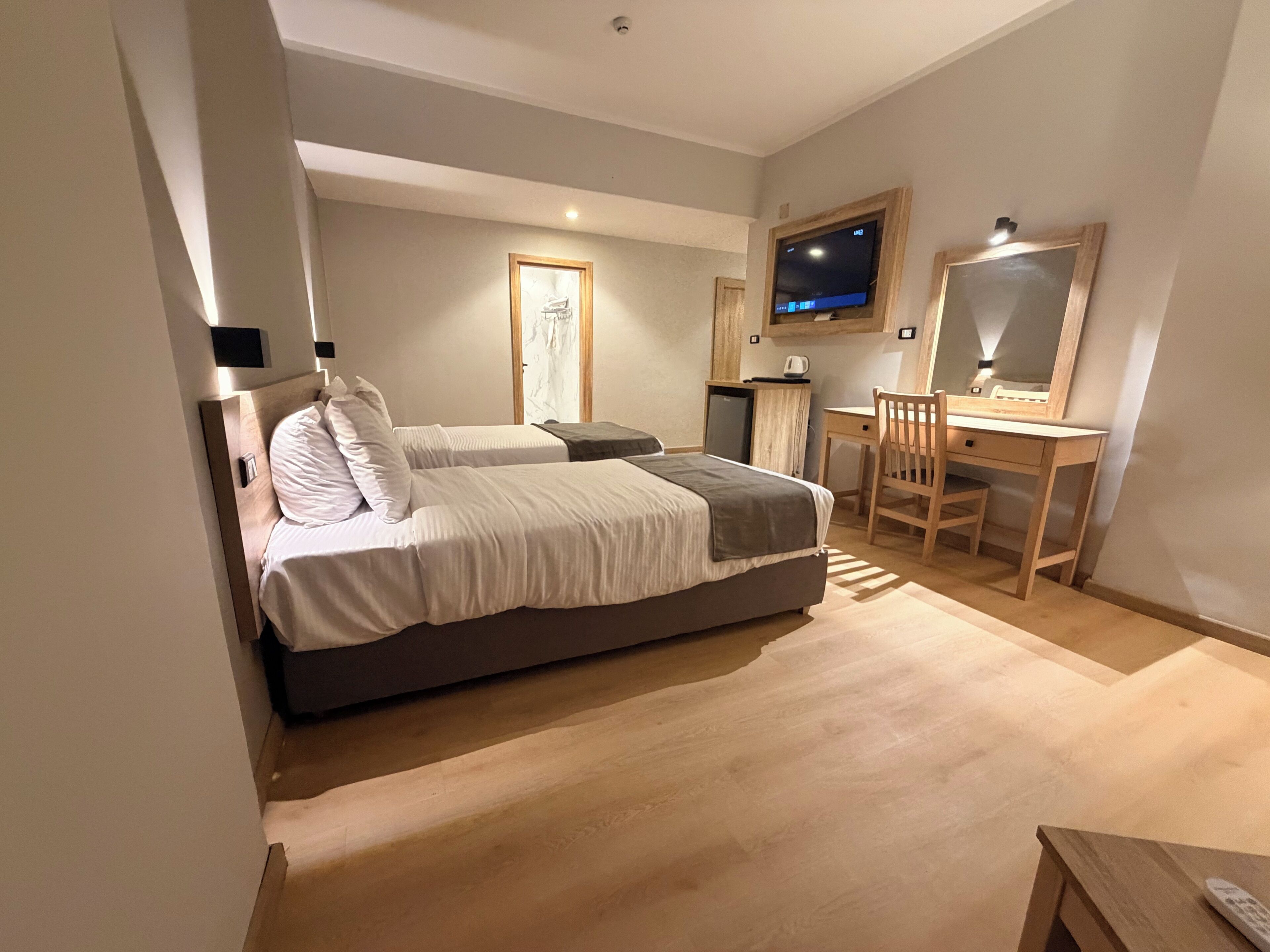A bedroom with two beds, a desk, a chair, a television, and a small refrigerator.