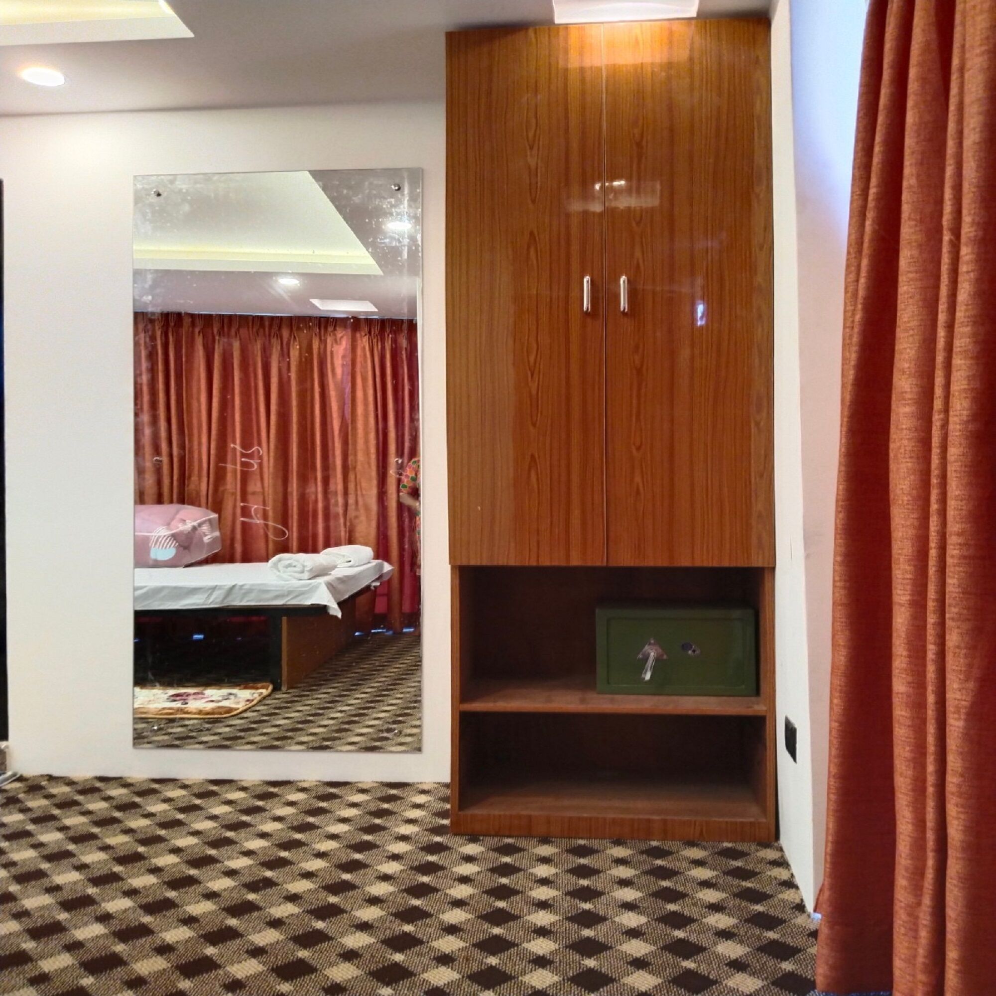A bedroom with a wooden wardrobe, a mirror, and a checkered carpet.