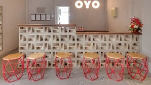 Ein Empfangsbereich mit einer Holztresen, roten geometrischen Hocker und einer Wand mit der leuchtenden Aufschrift "OYO".