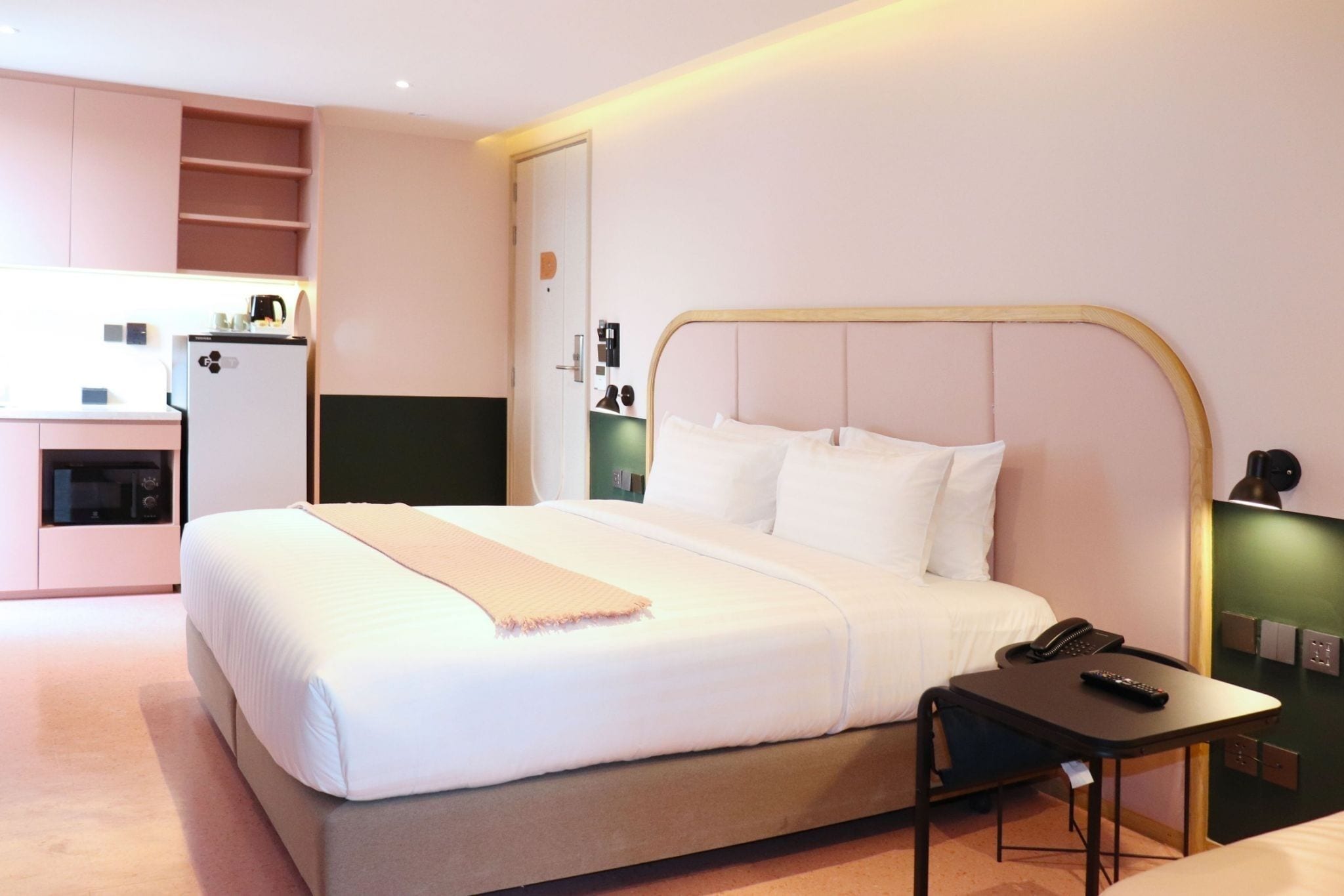 A hotel room with a bed, bedside table, and a small kitchenette area.