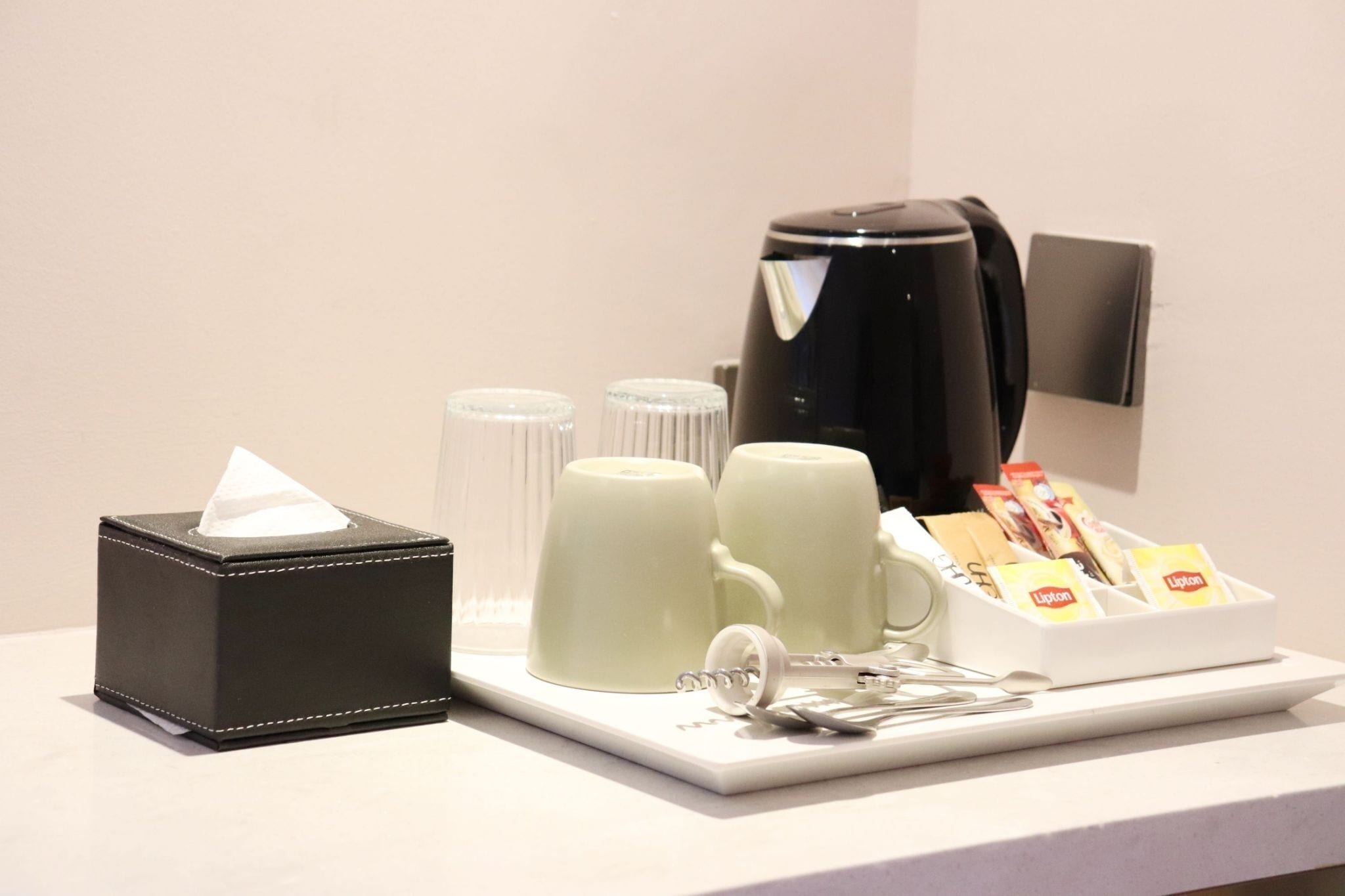 A hotel room's coffee station with a coffee maker, cups, a tissue box, and a Lipton tea dispenser.