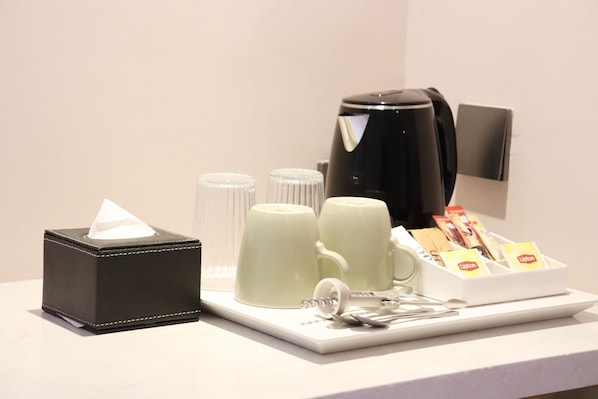 A hotel room's coffee station with a coffee maker, cups, a tissue box, and a Lipton tea dispenser.