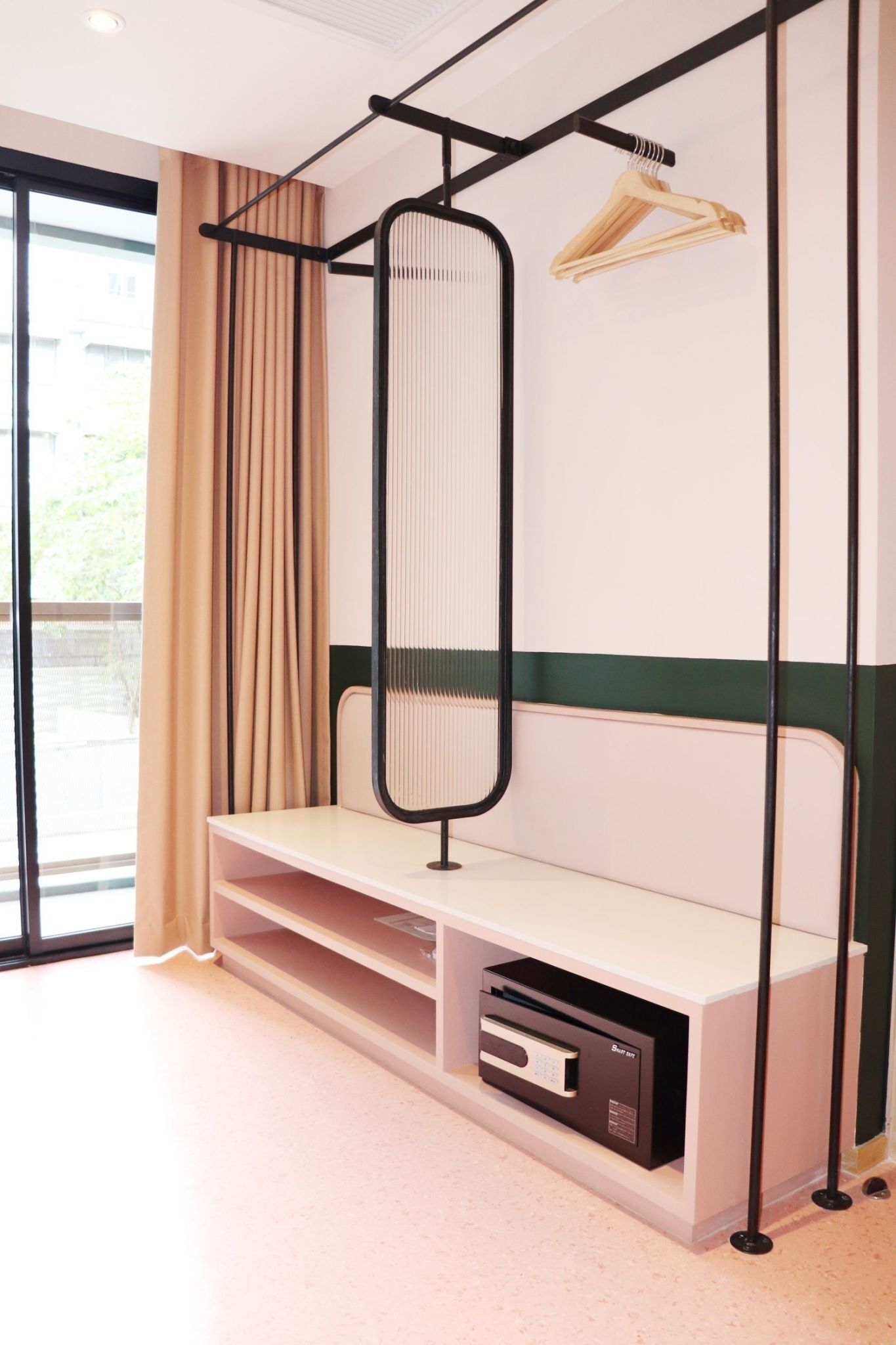 A room with a bed, a bench, a hanging rack, and a small shelf with a device.
