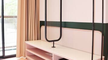 A room with a bed, a bench, a hanging rack, and a small shelf with a device.