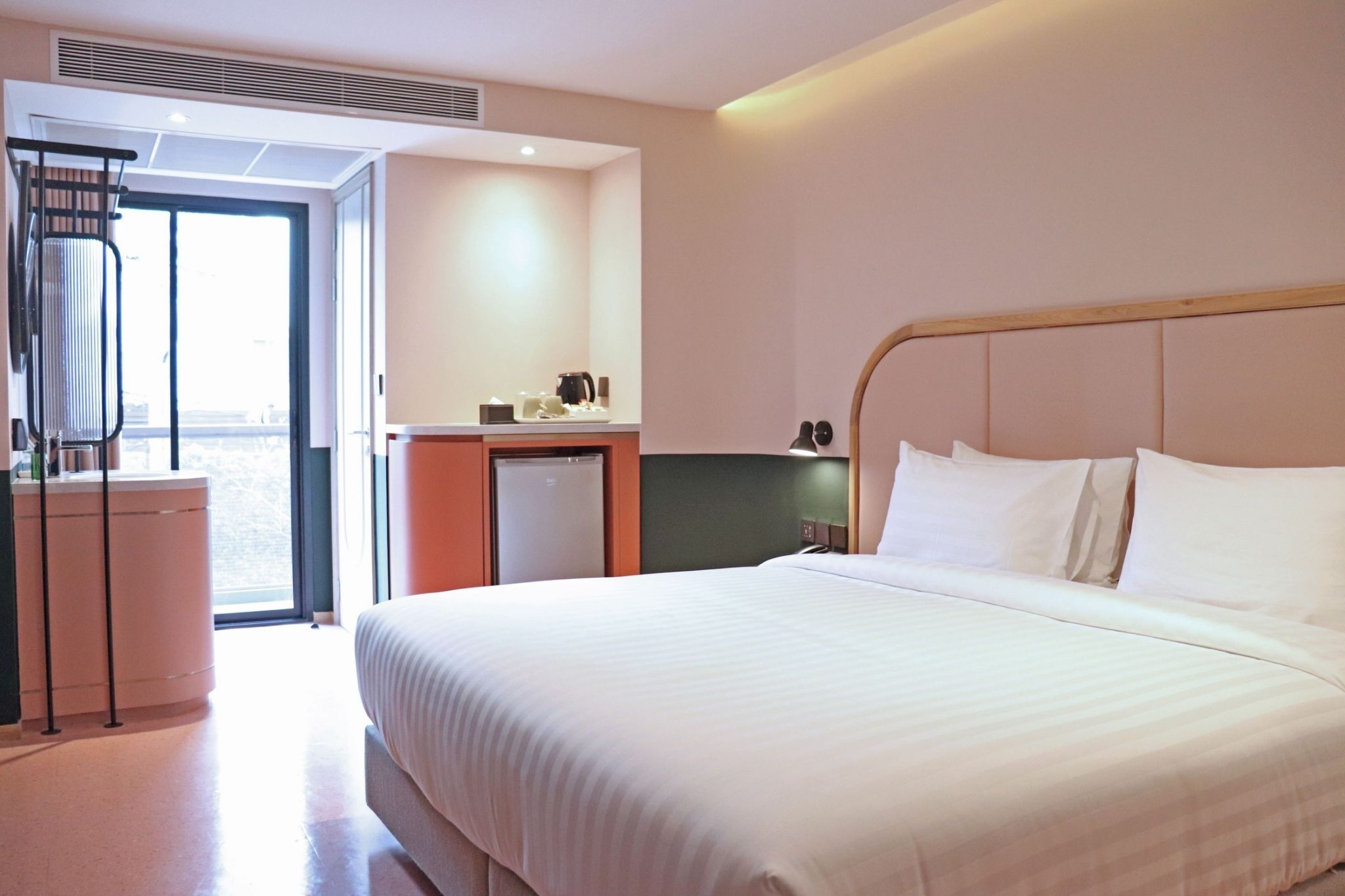 A hotel room with a large bed, a small kitchenette, a radiator, and a view through a glass door.