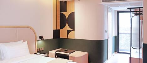 A hotel room with a large bed, a small desk, a chair, a mirror, and a window with a view of the outside.