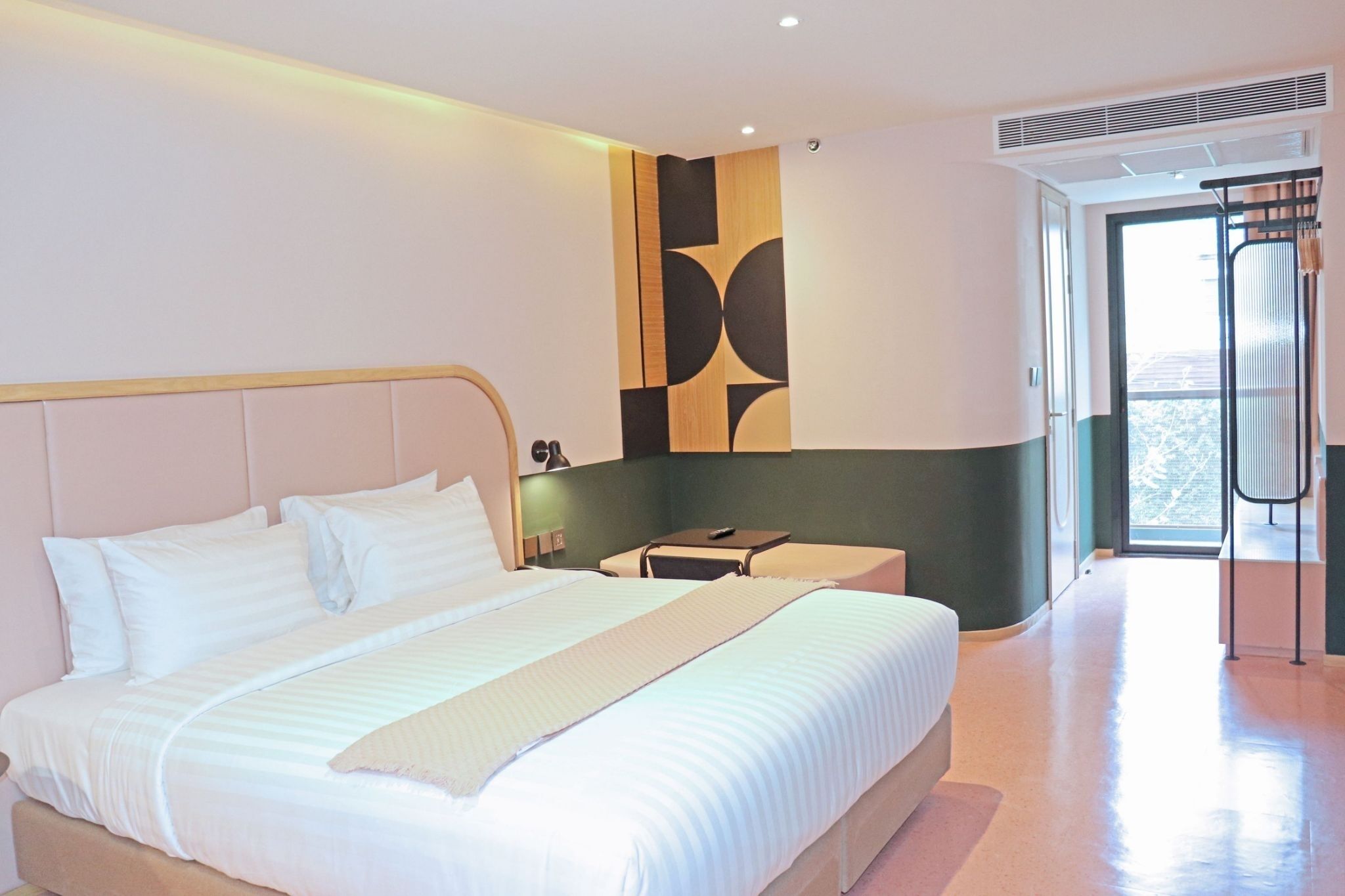 A modern hotel room with a large bed, a bedside table, a desk, and a view of the outdoors.