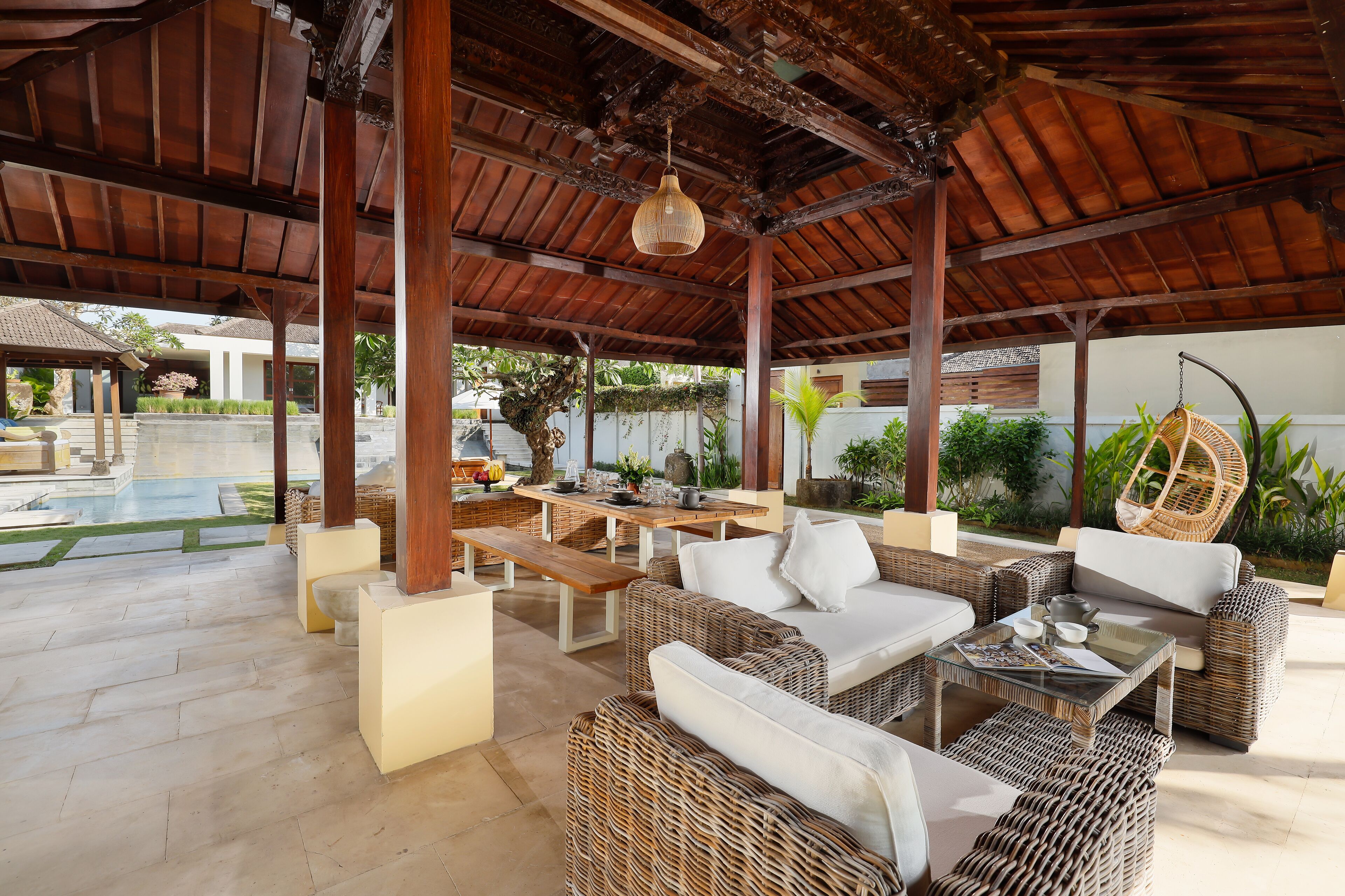 Eine Terrasse im Freien mit Korbmöbeln, einem Pool und einem überdachten Bereich mit einer Hängeleuchte.