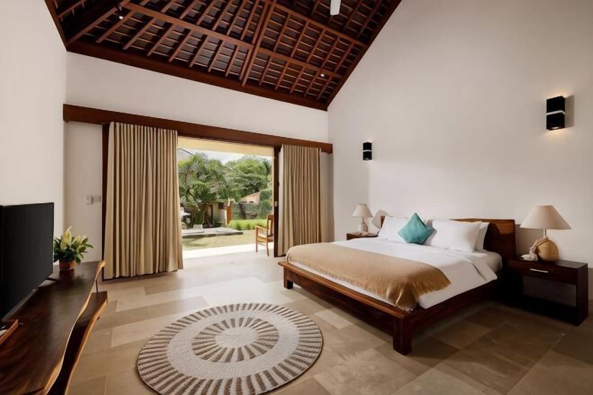 Un dormitorio con cama, mesitas de noche, televisor y vistas al exterior.