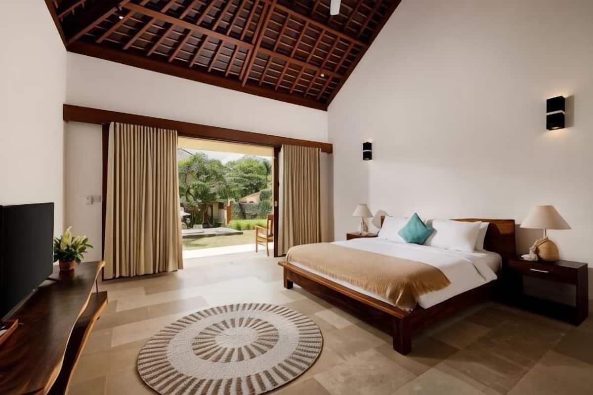 A bedroom with a bed, bedside tables, a TV, and a view of the outdoors.