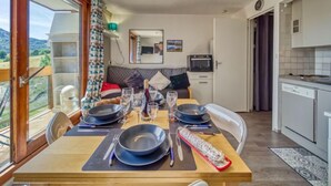 Ein Essbereich mit Tisch für vier Personen, eine Couch, eine Küche mit modernen Geräten und Blick ins Freie.