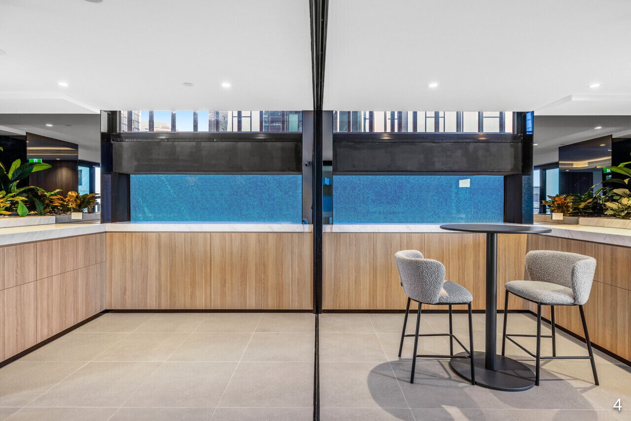 Un espacio interior moderno con un amplio panel de vidrio, dos sillones grises tapizados y una mesa redonda.