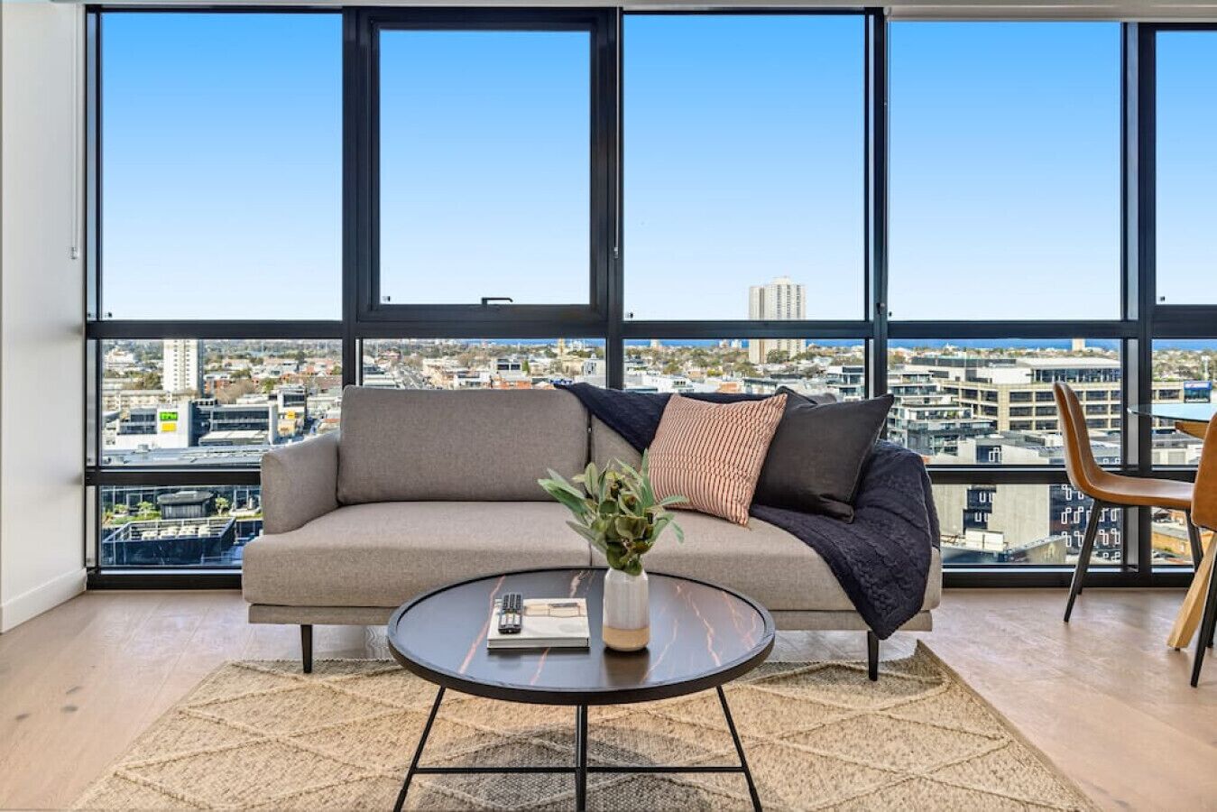 A modern living room with a sofa, a coffee table, and a view of a cityscape through large windows.