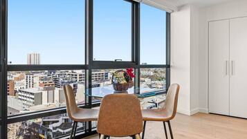 Una habitación moderna con ventanas amplias, una mesa de vidrio, dos sillas y vistas a la ciudad.