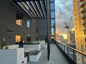 A modern building with a covered outdoor area, large windows, and a view of the city skyline.