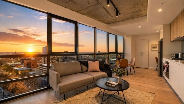 A modern living room with a large window, a sofa, a coffee table, and a kitchen area. - Spectacular Views, Comfort, Convenience. Gym, Pool, Rooftop, Tram, walk to Crown (Southbank)
