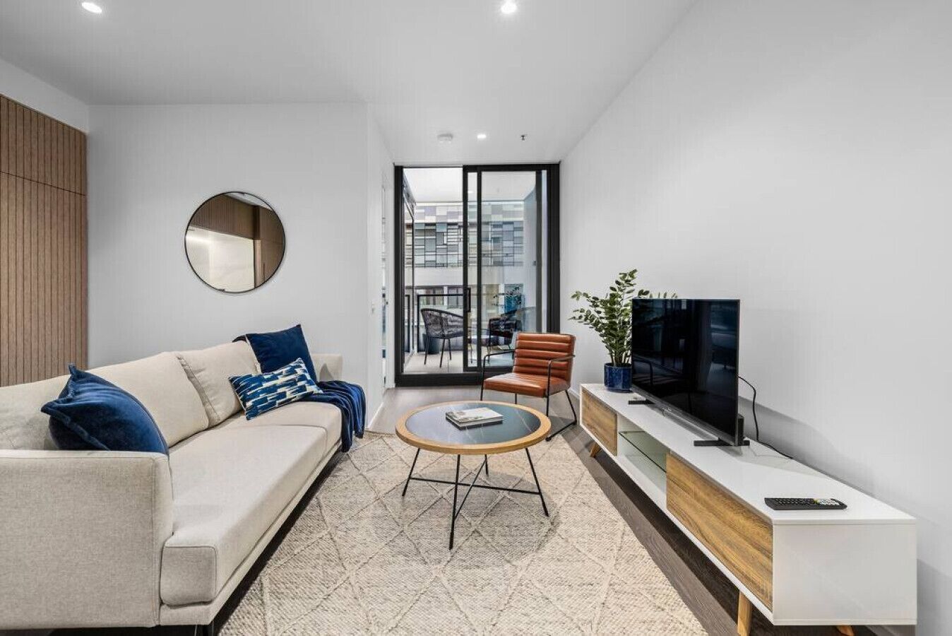 A modern living room with a sofa, coffee table, TV, and a view of the city through large windows.