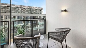 A balcony with two wicker chairs, a glass railing, and a view of a modern building with multiple floors. - The Park House City Retreat on the Yarra River (Abbotsford)
