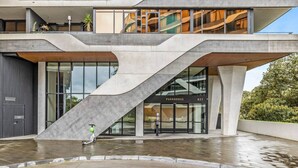 A modern building with a unique angular design, a visible entrance labeled "PARKHOUSE," and a person riding a scooter in front. - The Park House City Retreat on the Yarra River (Abbotsford)